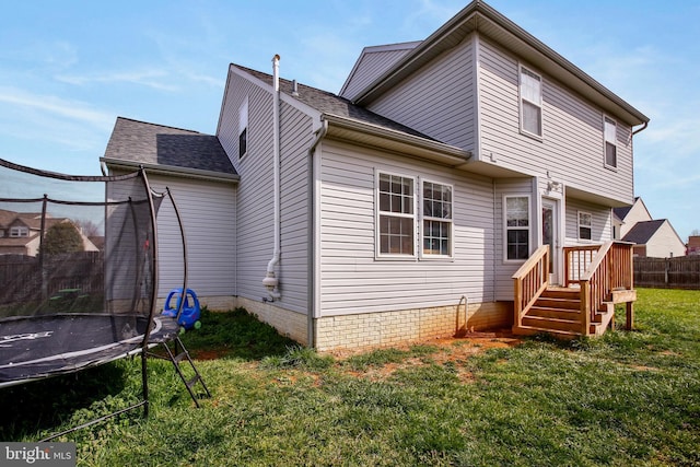 rear view of house with a lawn, fence, and a trampoline