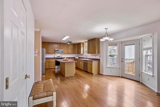 kitchen with an inviting chandelier, a kitchen island, pendant lighting, light wood finished floors, and appliances with stainless steel finishes