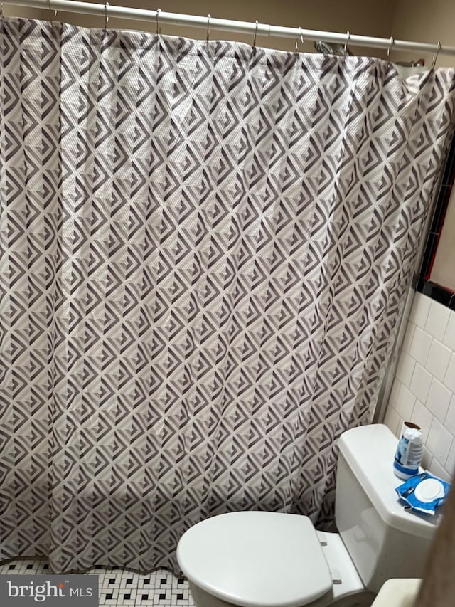 full bath featuring a shower with shower curtain, toilet, and tile walls
