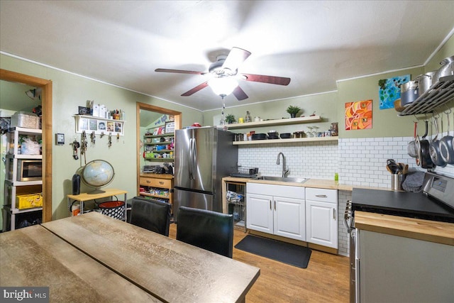 kitchen with butcher block countertops, freestanding refrigerator, white cabinets, ceiling fan, and a sink