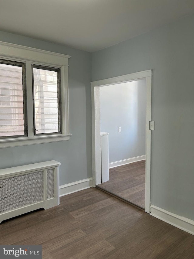 spare room featuring radiator heating unit, baseboards, and wood finished floors