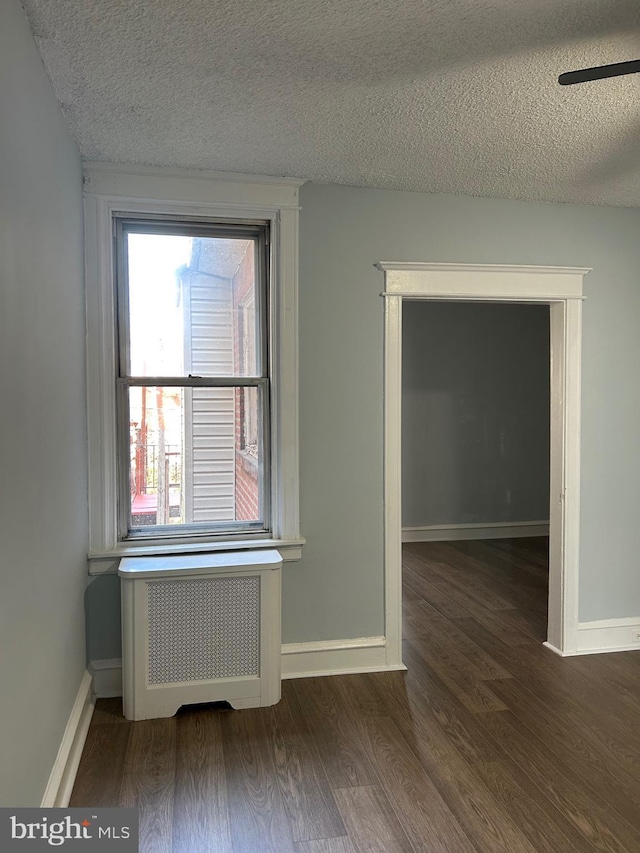 empty room featuring radiator, a textured ceiling, baseboards, and wood finished floors