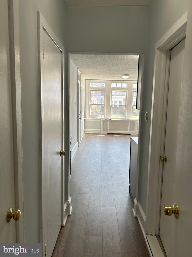 corridor with baseboards, a textured ceiling, and wood finished floors
