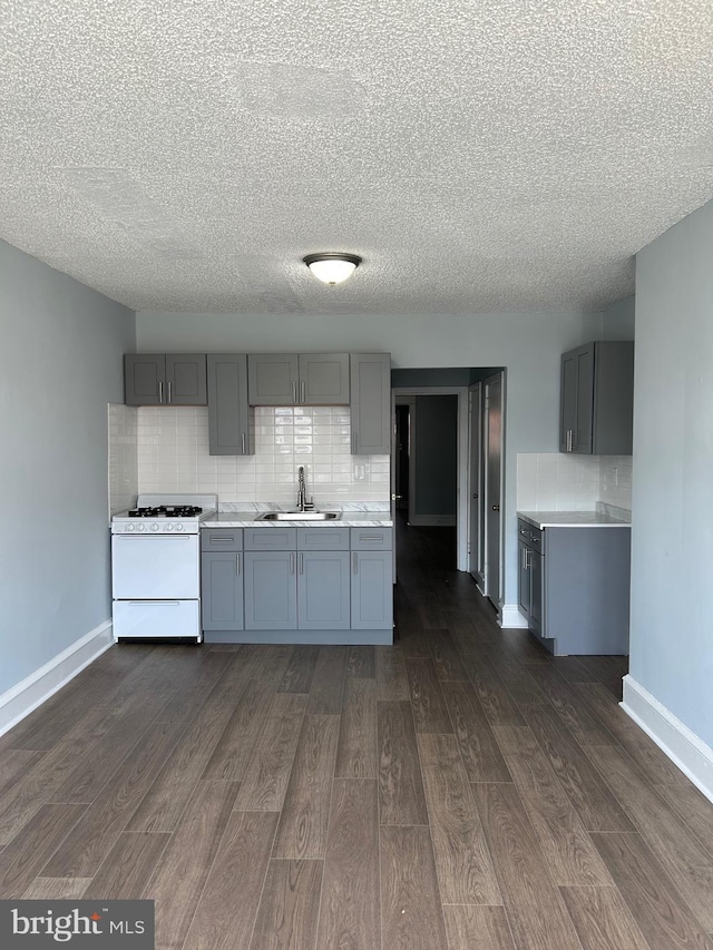 kitchen featuring gray cabinetry, light countertops, a sink, and white gas range oven