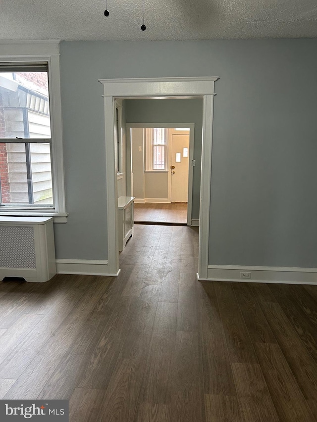 hall featuring a textured ceiling, dark wood-style floors, baseboards, and radiator