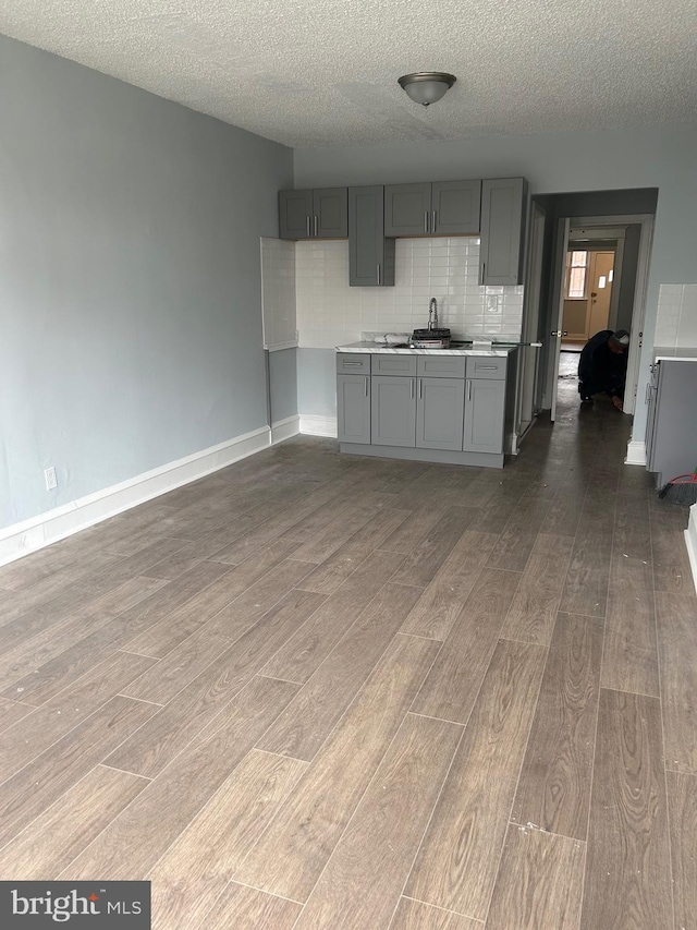 kitchen featuring light countertops, gray cabinets, backsplash, a sink, and wood finished floors