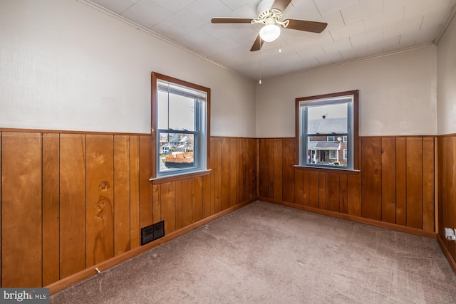 unfurnished room with ceiling fan, a healthy amount of sunlight, and wainscoting