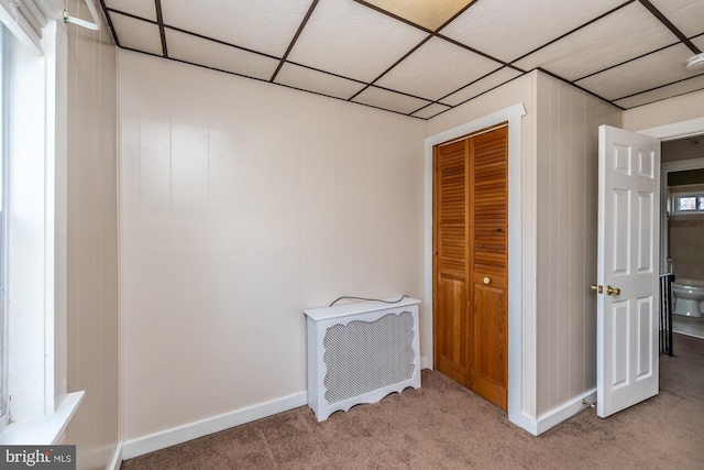 unfurnished bedroom featuring baseboards, a closet, carpet floors, and a drop ceiling