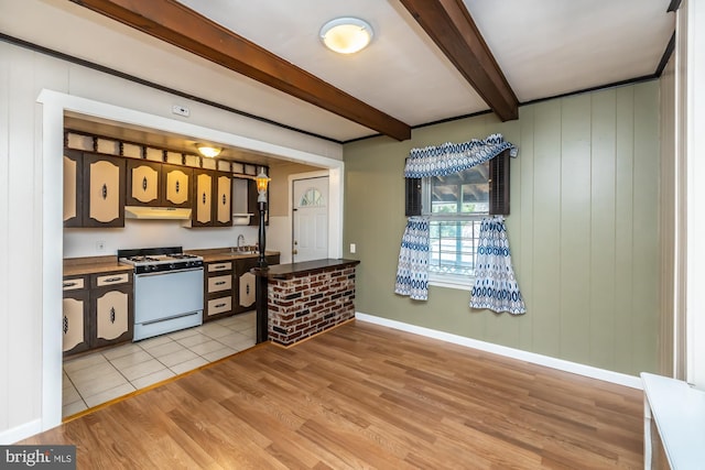 kitchen with beamed ceiling, under cabinet range hood, a sink, gas range gas stove, and light wood-style floors