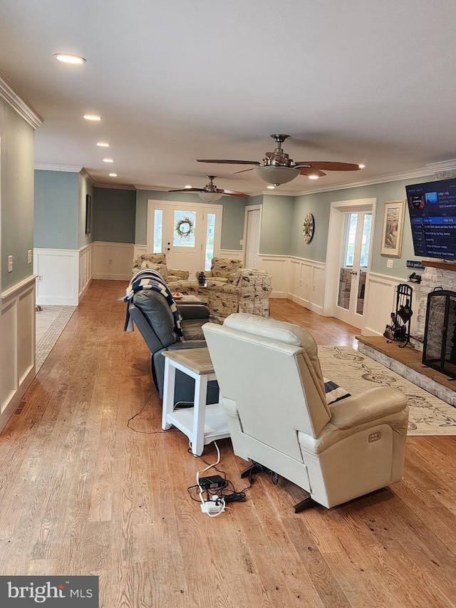 living room with crown molding, ceiling fan, wainscoting, and light wood-style flooring