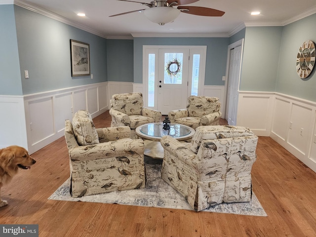 living room featuring a decorative wall, a ceiling fan, crown molding, wood finished floors, and a wainscoted wall