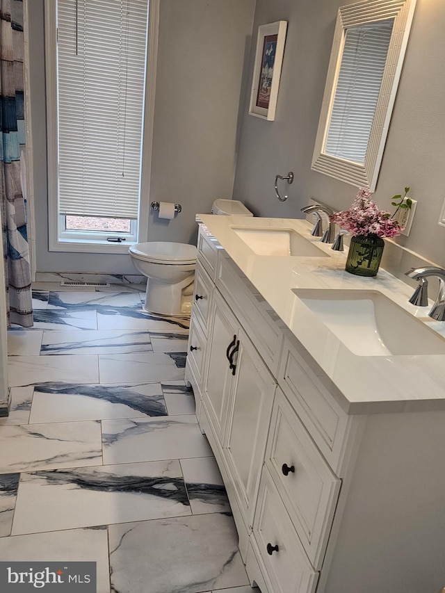 full bath featuring a sink, toilet, double vanity, and marble finish floor