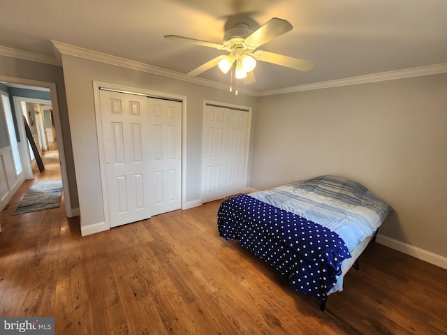 bedroom featuring ornamental molding, two closets, and wood finished floors