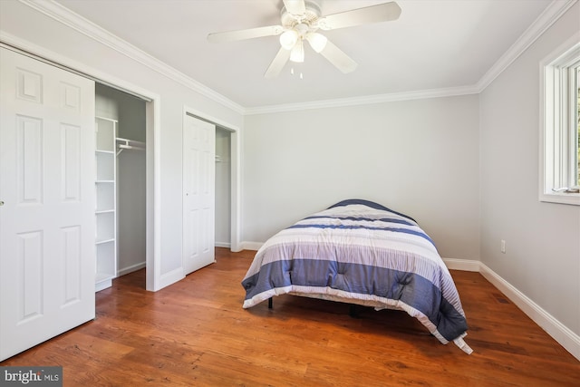 bedroom with a ceiling fan, crown molding, wood finished floors, multiple closets, and baseboards