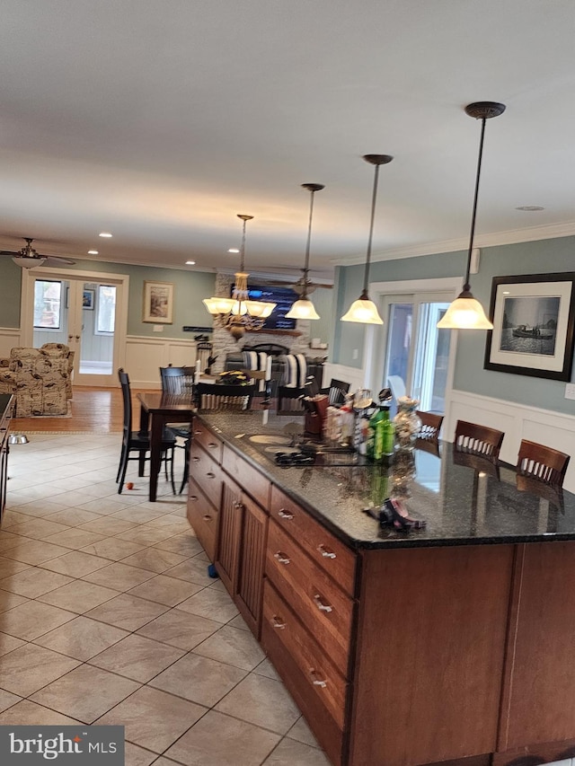kitchen featuring hanging light fixtures, crown molding, dark stone counters, a kitchen island, and light tile patterned flooring