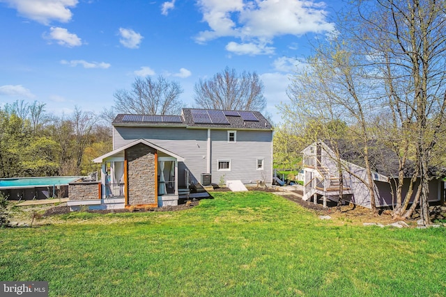 back of property featuring an outdoor pool, central AC unit, a lawn, and roof mounted solar panels