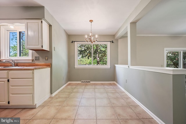 unfurnished dining area featuring a sink, light tile patterned flooring, a notable chandelier, and a wealth of natural light