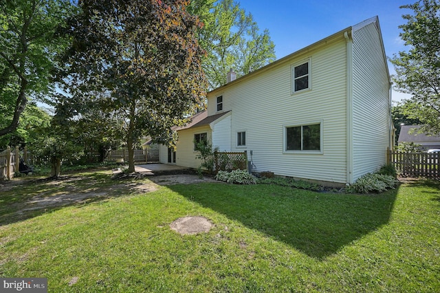 rear view of property featuring a patio, a fenced backyard, a yard, and a chimney
