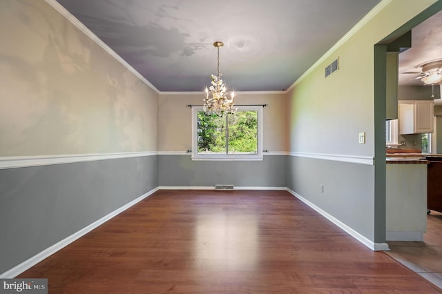 unfurnished dining area featuring crown molding, ceiling fan with notable chandelier, wood finished floors, and visible vents
