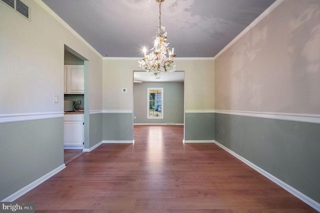 unfurnished dining area with visible vents, ornamental molding, wood finished floors, and a notable chandelier