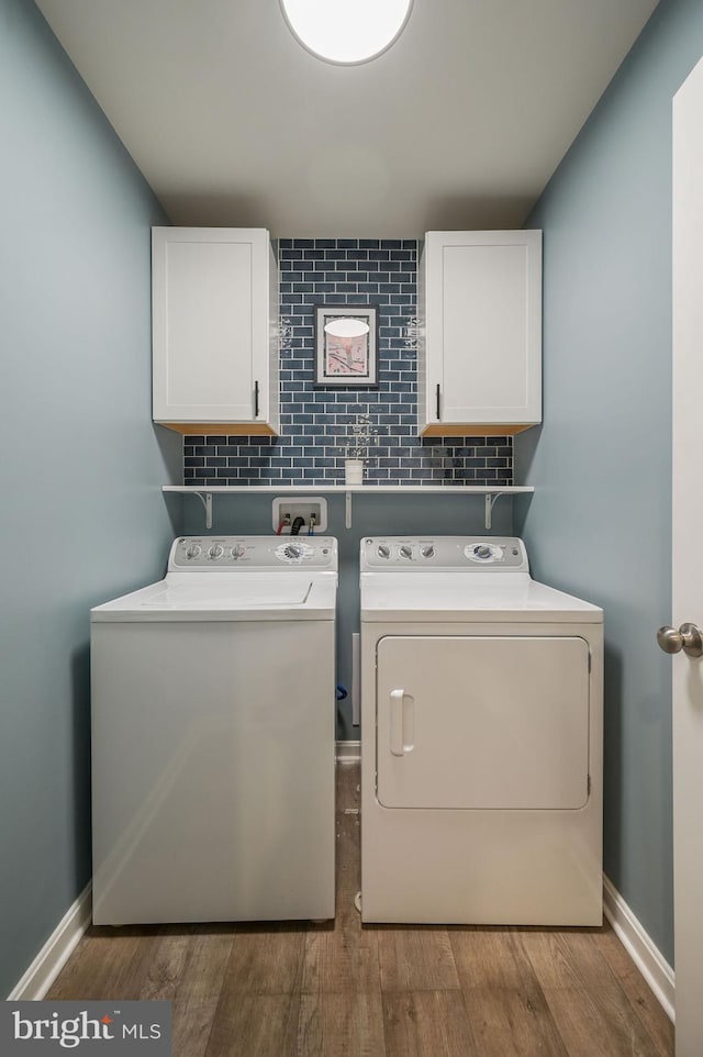 washroom featuring washing machine and dryer, baseboards, cabinet space, and wood finished floors