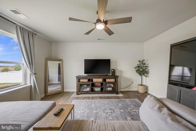 living room featuring wood finished floors, visible vents, baseboards, and ceiling fan