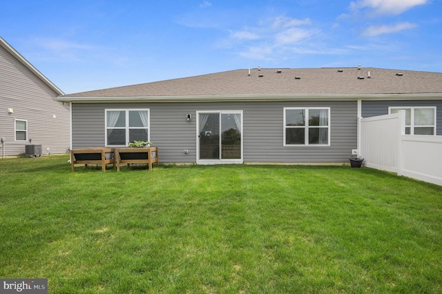 back of property featuring central AC unit, fence, a yard, and a shingled roof