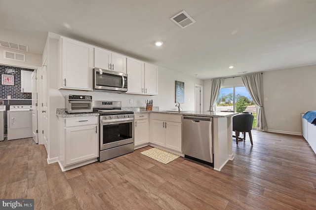 kitchen featuring washer and clothes dryer, white cabinetry, a peninsula, appliances with stainless steel finishes, and visible vents