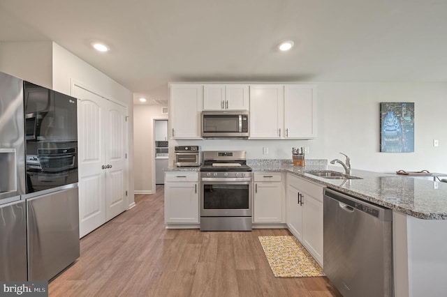 kitchen featuring white cabinets, stone counters, appliances with stainless steel finishes, and a sink
