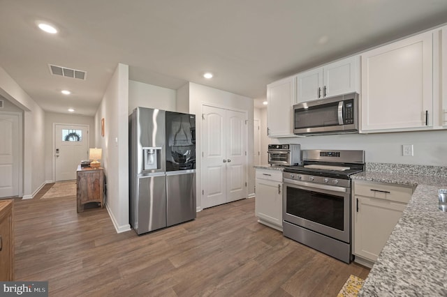 kitchen with visible vents, white cabinetry, wood finished floors, light stone counters, and appliances with stainless steel finishes