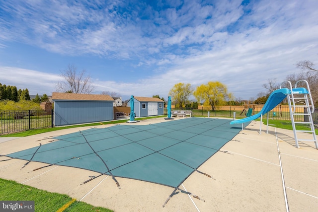 view of pool featuring a water slide, fence, an outbuilding, a storage shed, and a patio
