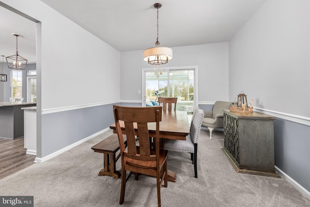 carpeted dining room with a chandelier and baseboards