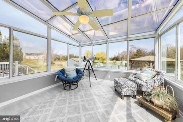 sunroom / solarium featuring a ceiling fan, baseboards, wood finished floors, and an outdoor hangout area
