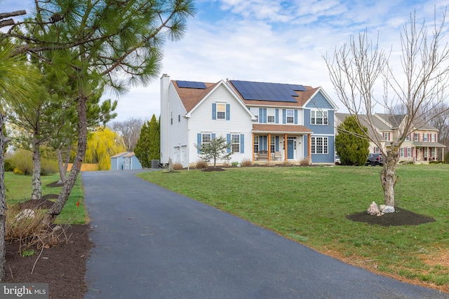 traditional-style home featuring covered porch, a chimney, a front lawn, and solar panels