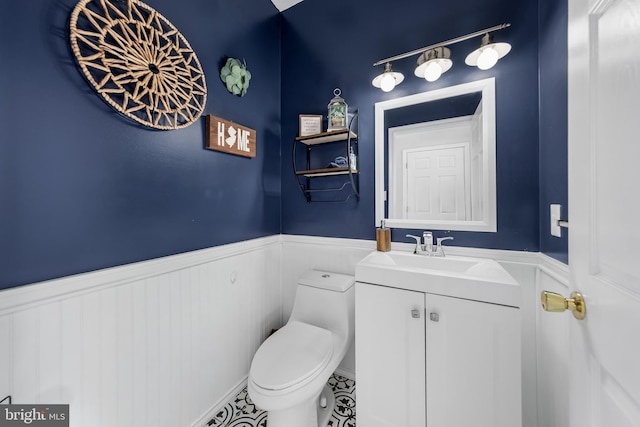 half bathroom with a wainscoted wall, toilet, vanity, and tile patterned floors