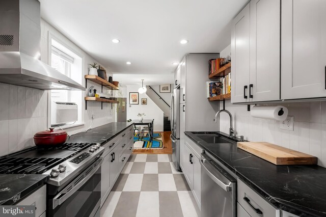 kitchen with open shelves, stainless steel appliances, wall chimney exhaust hood, a sink, and recessed lighting