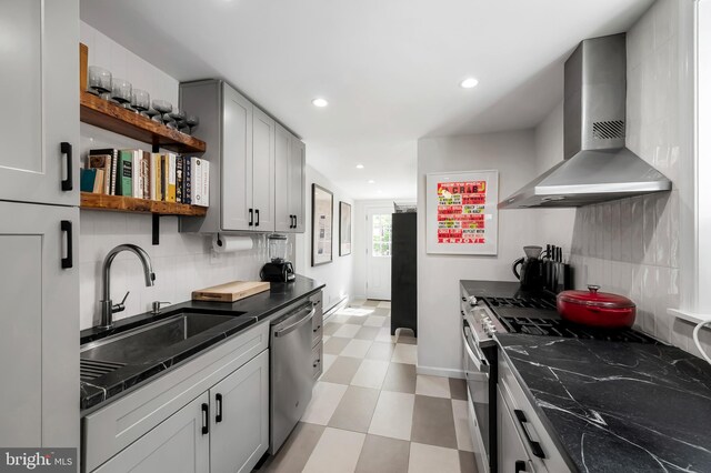 kitchen featuring wall chimney exhaust hood, open shelves, appliances with stainless steel finishes, a sink, and backsplash