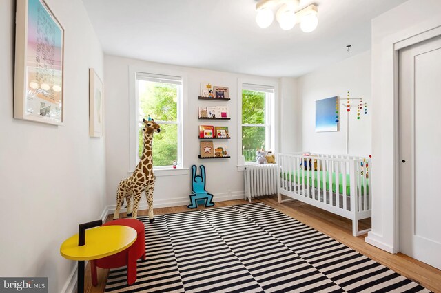bedroom featuring radiator heating unit, wood finished floors, a nursery area, and baseboards