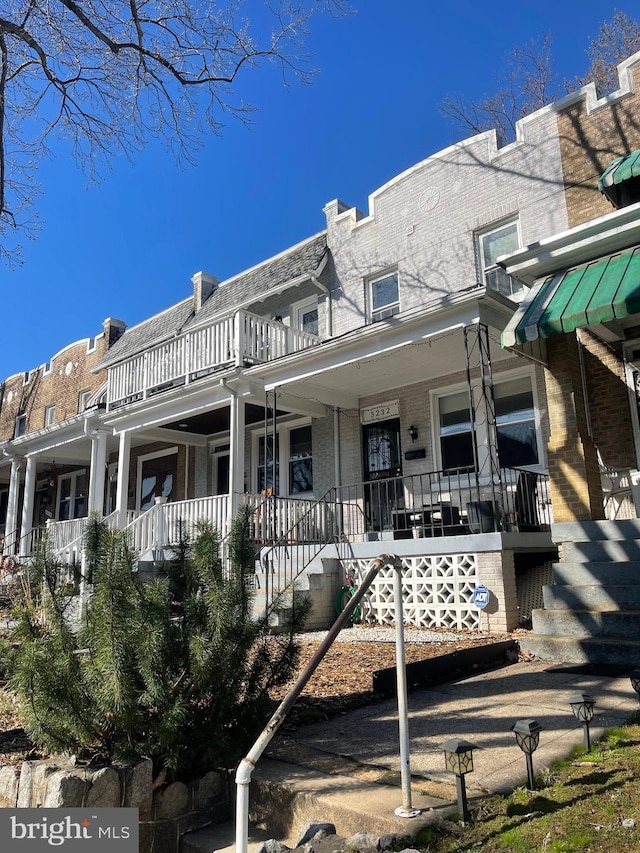 rear view of property featuring brick siding, a balcony, stairway, and covered porch