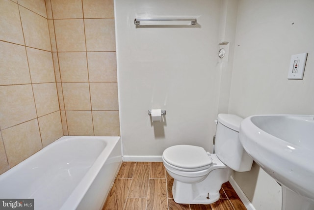 bathroom featuring a washtub, wood finish floors, a sink, baseboards, and toilet