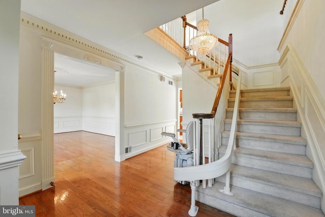 stairs featuring wood finished floors, an inviting chandelier, and a decorative wall