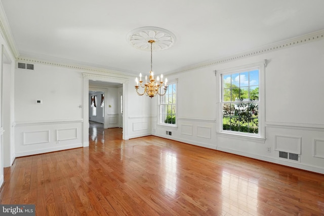 unfurnished dining area with a decorative wall, wood finished floors, visible vents, and a notable chandelier
