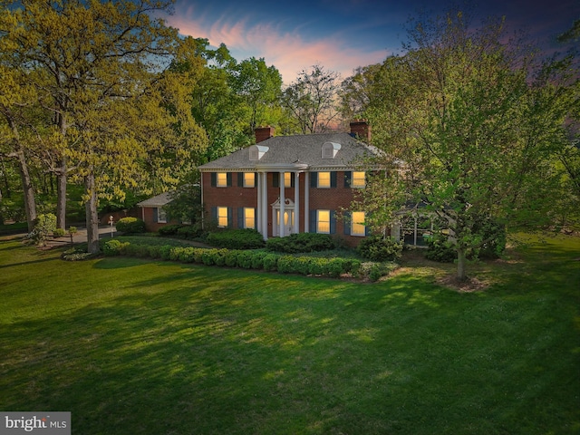 view of front of house featuring a front lawn, a chimney, and brick siding