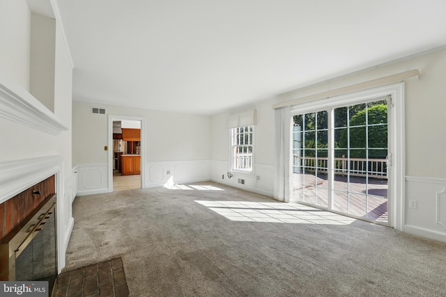 unfurnished living room with a decorative wall, carpet floors, a healthy amount of sunlight, and wainscoting