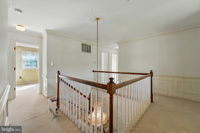 hall with a decorative wall, visible vents, light carpet, and an upstairs landing