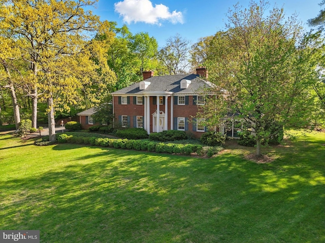 neoclassical / greek revival house featuring a chimney, brick siding, and a front yard