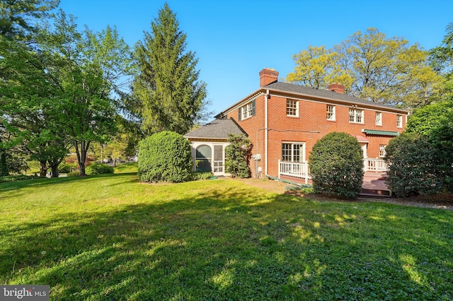 back of house with a chimney, a wooden deck, brick siding, and a lawn