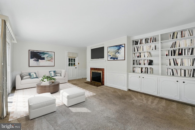 living room with a decorative wall, wainscoting, built in features, carpet, and a brick fireplace