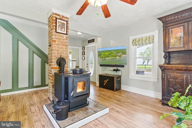 living area with a textured ceiling, a wood stove, ceiling fan, light wood-style floors, and baseboards