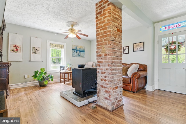 living area featuring wood finished floors, baseboards, a wood stove, a ceiling fan, and a textured ceiling